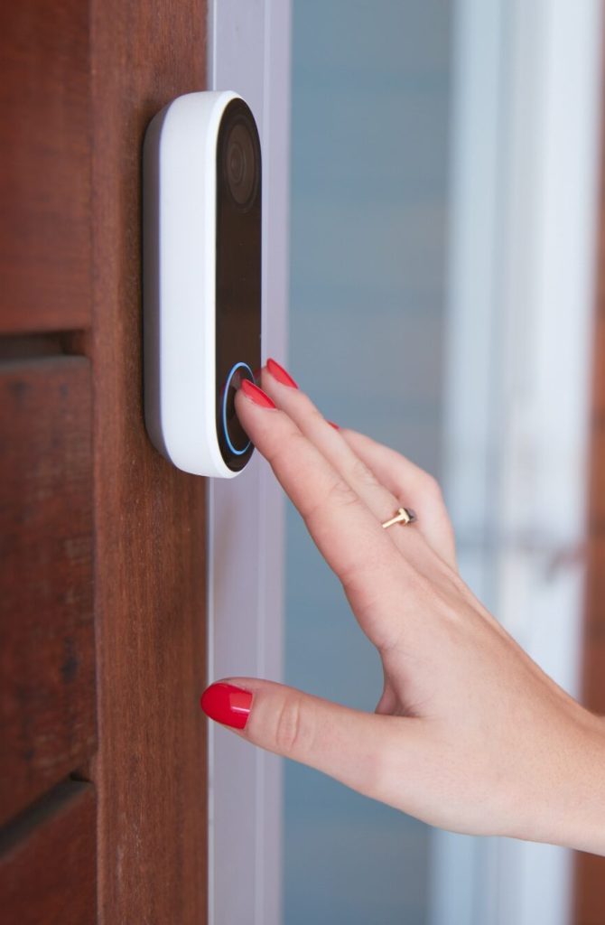 Close Up Of Woman Ringing Front Doorbell Equipped With Security Video Camera